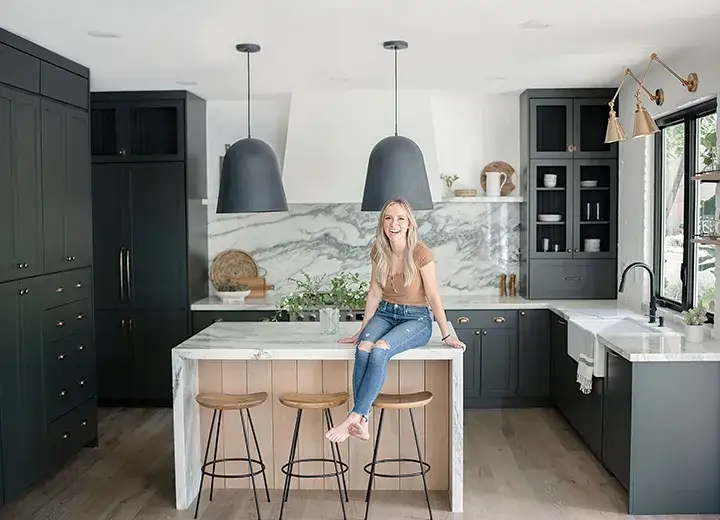 Angela Rose Home DIY Collection A photo of Angela Rose sitting on her kitchen island, smiling, surrounded by a kitchen updated with Dream Dusk Slim Shaker cabinet doors.