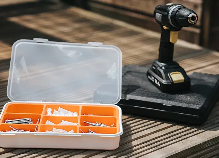 A picture of a power screwdriver with an open box of screws on a table.