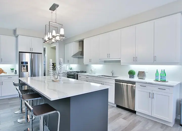 An image of a kitchen with white Valu-Line shaker cabinet doors, a dark blue island, and brushed nickel hardware and lighting.