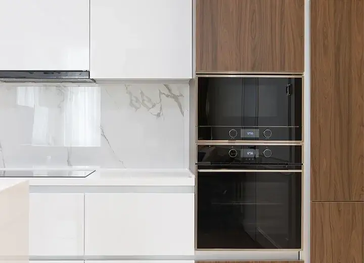 A picture of a kitchen with wood grain walnut cabinet doors next to white slab cabinet doors, beside an oven stack.