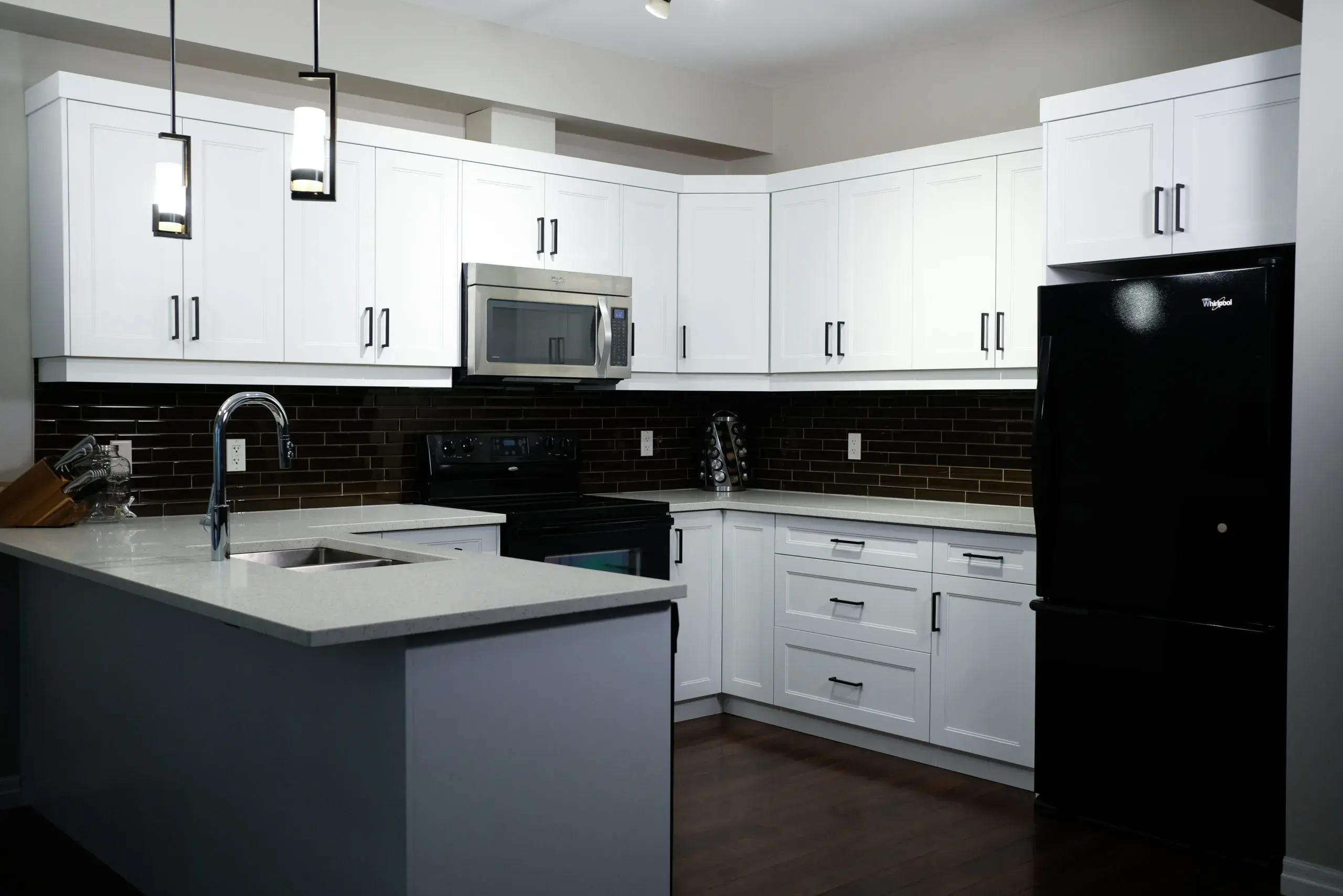 A photo of a kitchen with white shaker cabinet doors, black appliances, and quartz countertops.