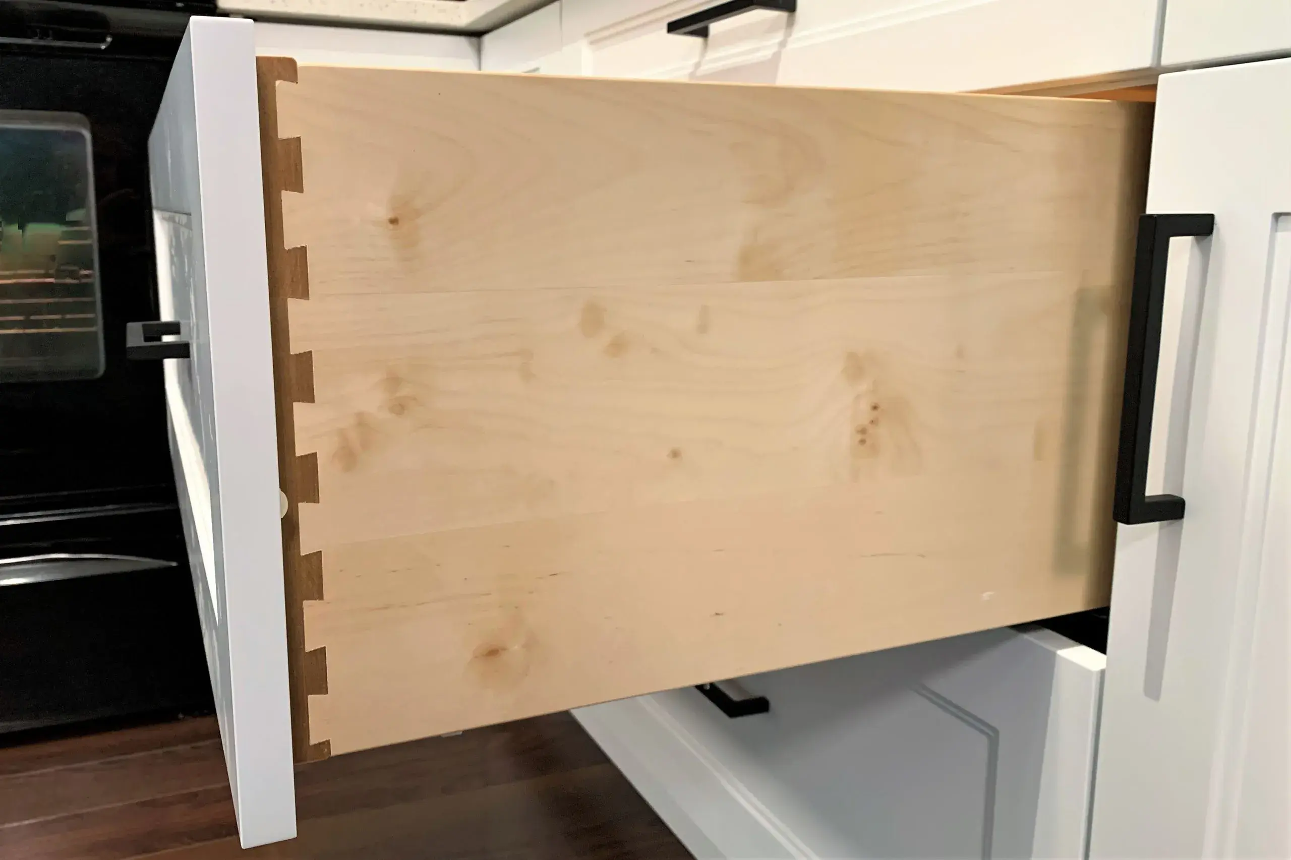 A photo of the side of a wooden dovetail drawer box showing the dovetail joinery, with a white drawer front attached.