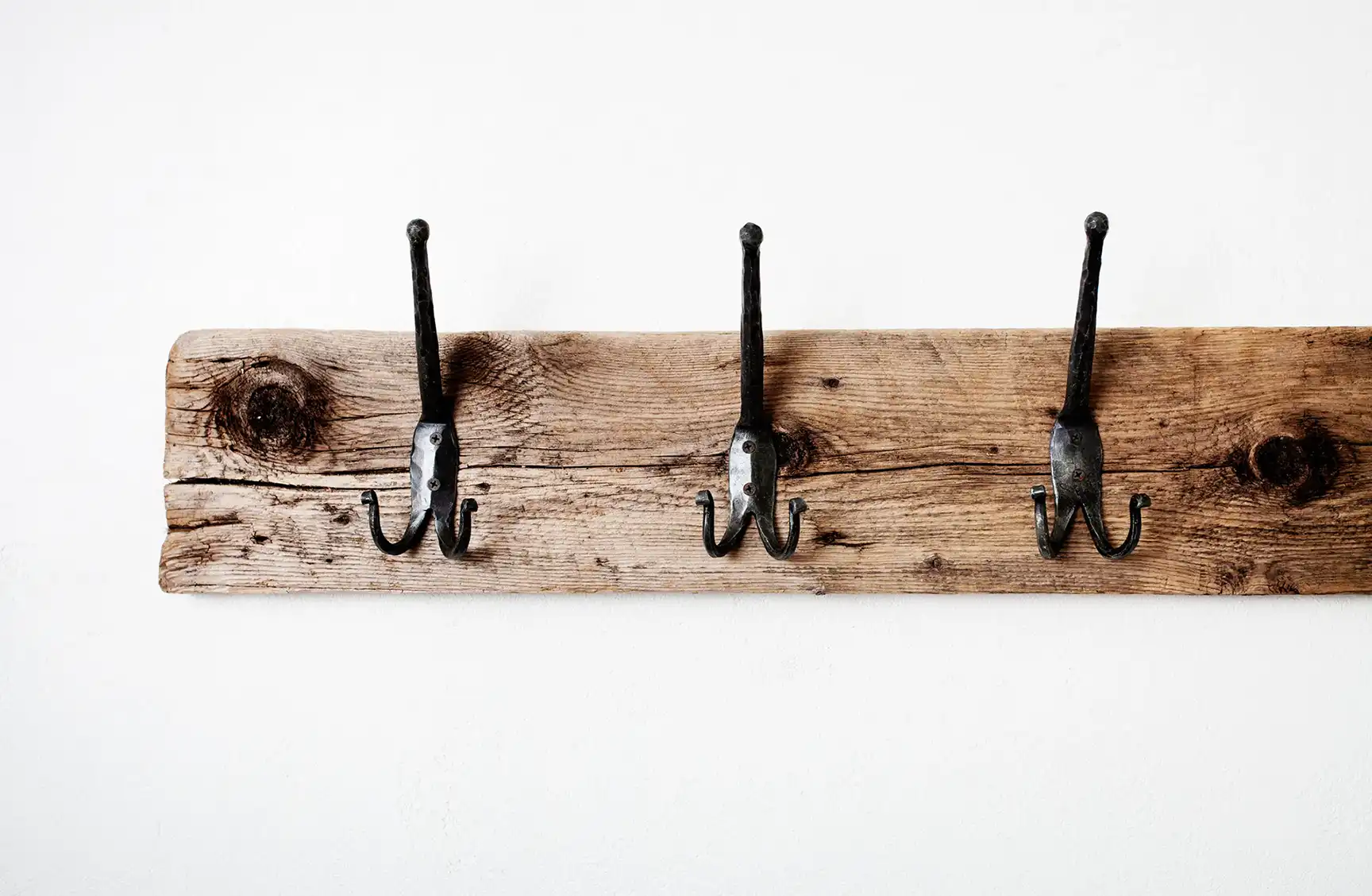 An image of three black hooks mounted on a rustic piece of wood.