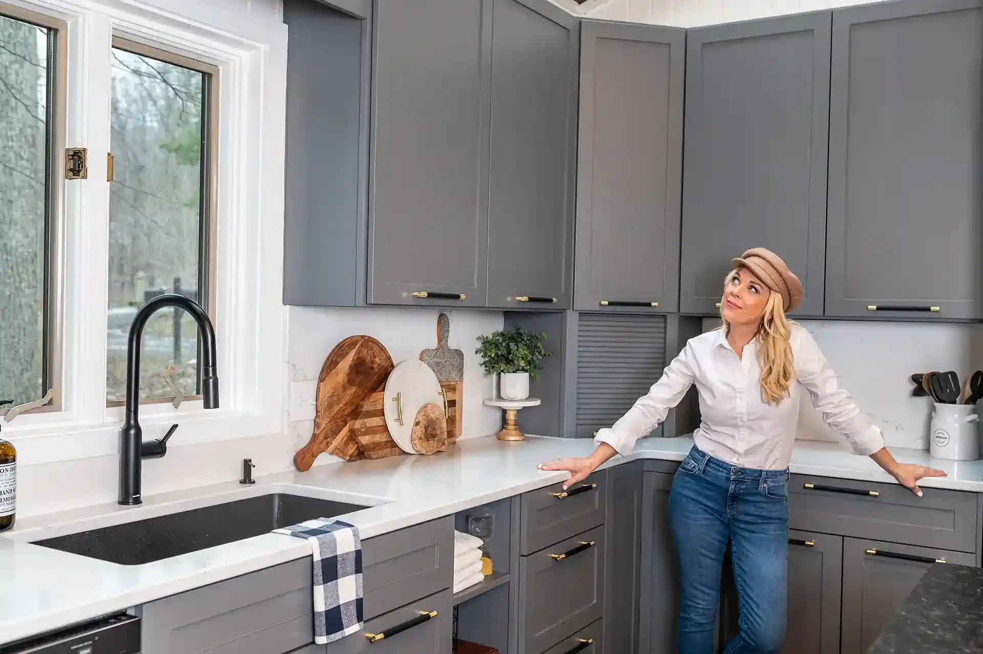 A picture of Kortney Wilson in her updated Lake House kitchen with grey cabinetry and white quartz countertops.