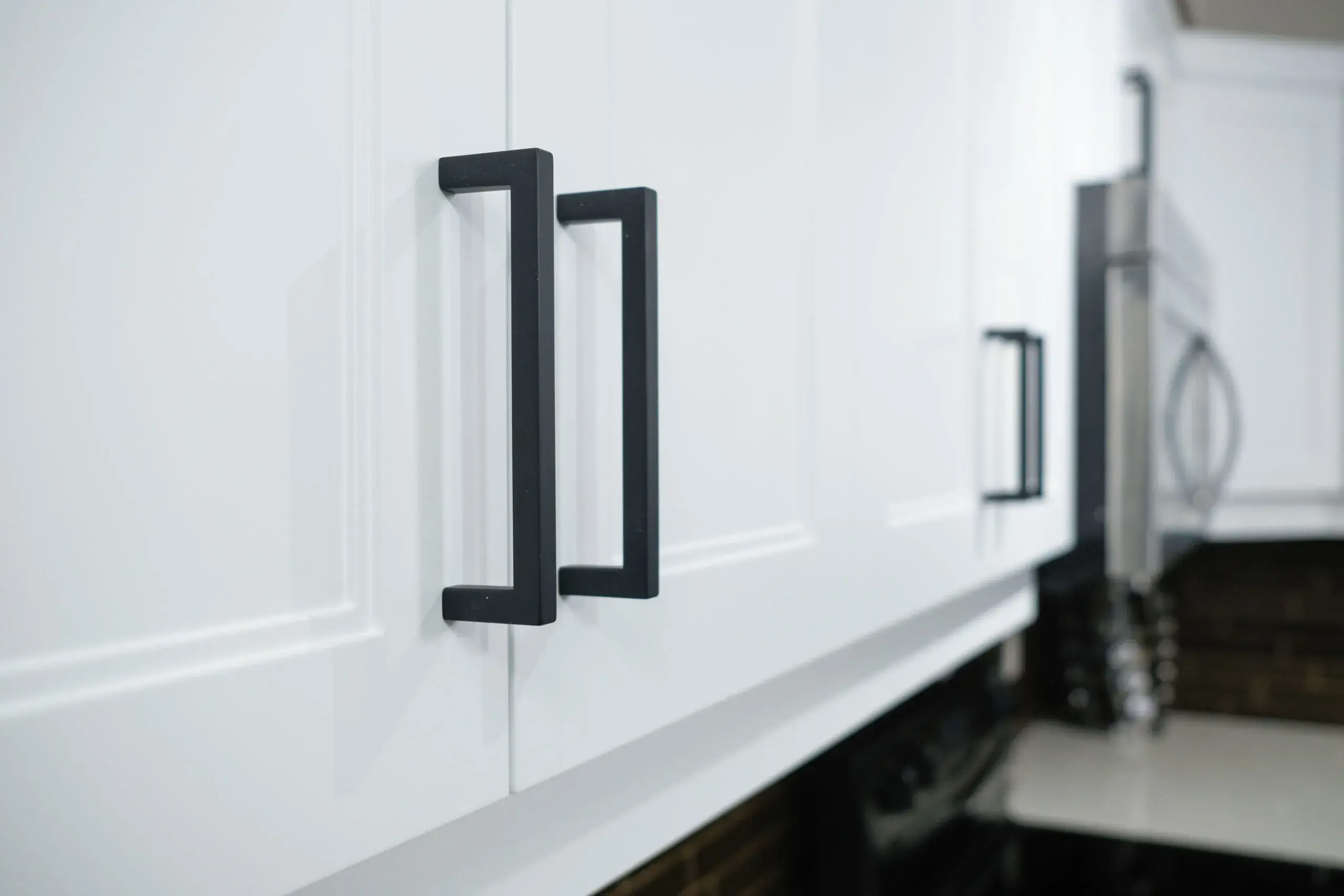 A photo of modern white shaker cabinet doors with black handles.