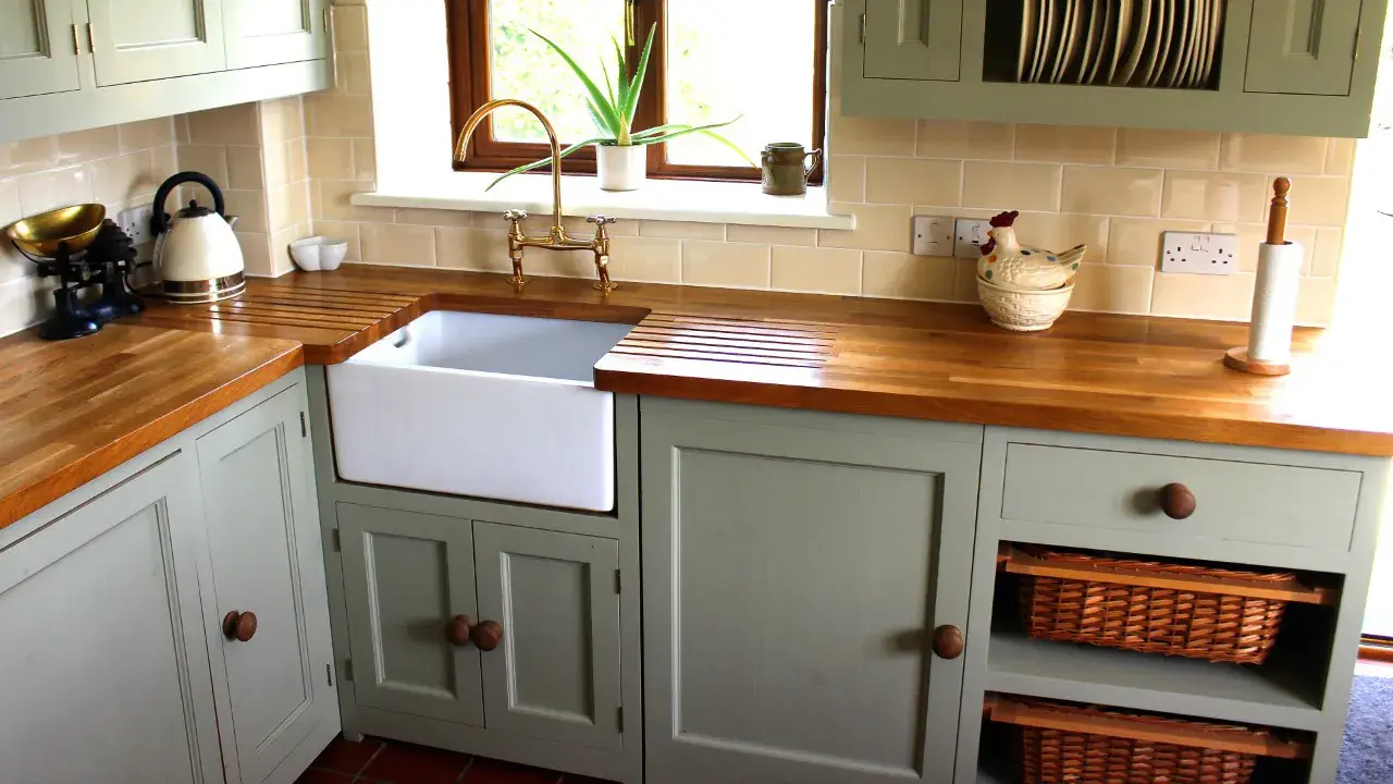A photo of a kitchen with grey painted cabinet doors, a white farmhouse sink, and butcher block countertops.