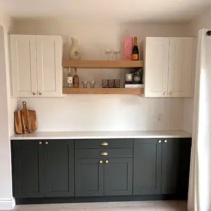 An image of a dry-bar area in a dining room with shaker style cabinetry, Dream Dusk base cabinets and Warm White uppers. The upper cabinets are connected by two wooden floating shelves.