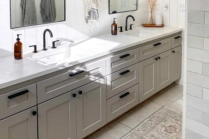 An image of a bathroom vanity with shallow shaker cabinet doors in taupe. Matte black hardware and faucets accent the concrete countertops.