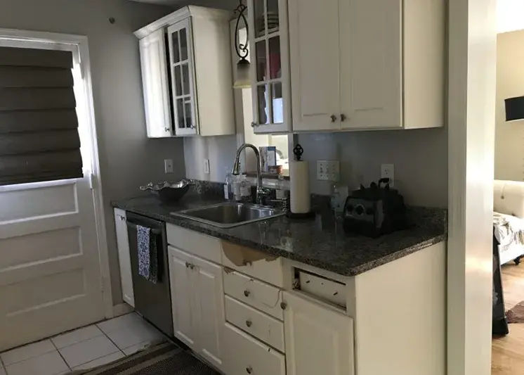 A photo of a kitchen with broken and damaged cabinet doors.