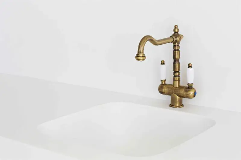 A closeup image of a brass kitchen faucet with white handles.