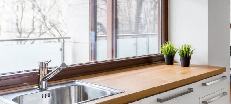 An image of a wooden butcher block countertop with white slab cabinet doors and a chrome faucet.