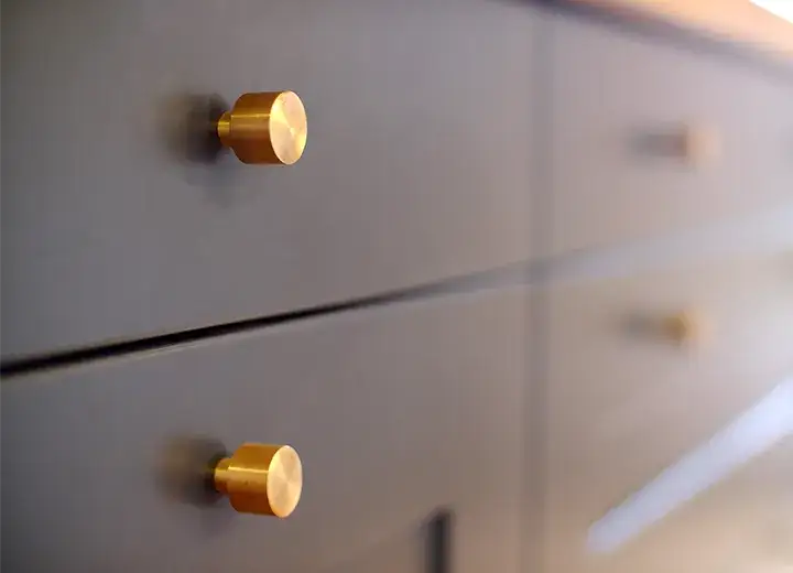 A closeup photo of navy blue drawer fronts with brass knobs.