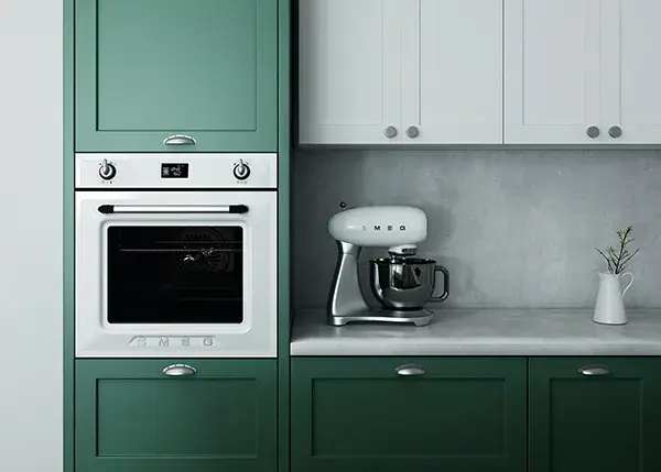 An image of green and white shaker style kitchen with a white stand mixer on the countertop and a stainless steel oven.