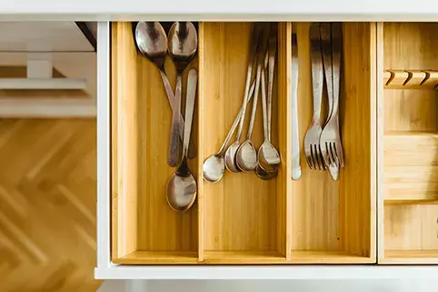 A photo of an open kitchen drawer with wooden cutlery organizer.