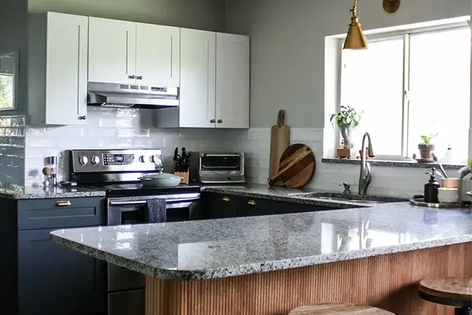 An image of a kitchen with white upper cabinets, dark green base cabinets, and a wood island. Brass lighting and hardware are visible as accents.