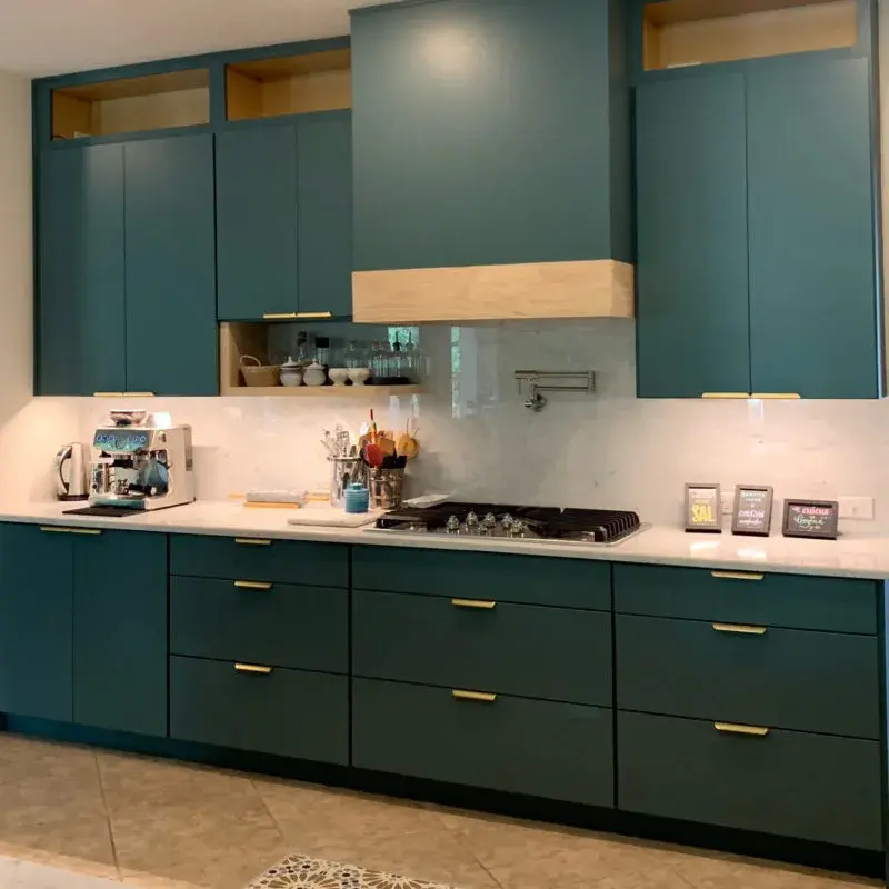 An image of a contemporary kitchen with sage green slab cabinet doors, wooden trim on the range hood, and quartz countertops.