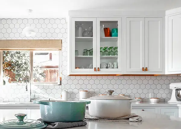 A kitchen with white shaker cabinet doors, with two glass cabinet doors and leather cabinet pulls.