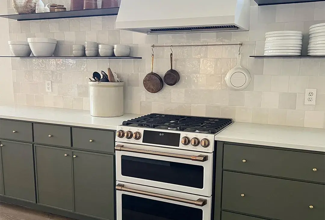 A kitchen with contemporary skinny shaker cabinet doors in an olive green colour with floating shelves on both sides of a plaster range hood.