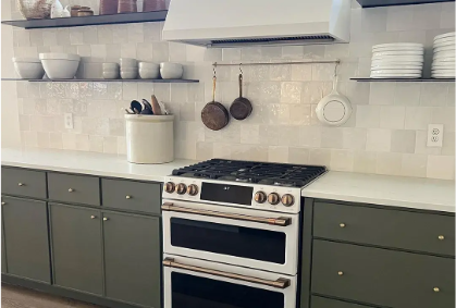 A kitchen with contemporary skinny shaker cabinet doors in an olive green colour with floating shelves on both sides of a plaster range hood.