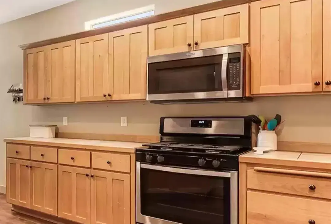 An image of a kitchen with dated double panelled shaker style golden oak cabinet doors.