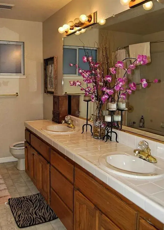 An image of a bathroom with old oak vanity, tile countertops, brassy lighting, and a purple orchid on the countertop.