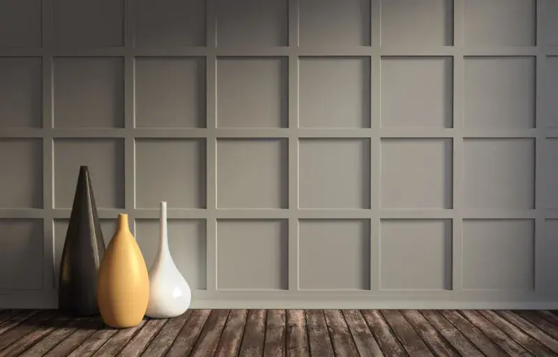 An image of a taupe accent wall with a checkered board and batten pattern, with decorative vases on the floor.