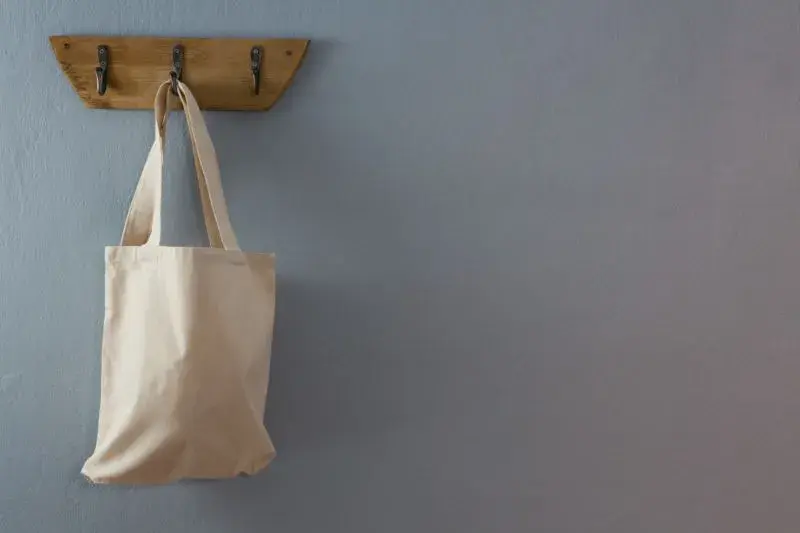 An image of a canvas bag hanging from a wood and metal rustic wall hook.
