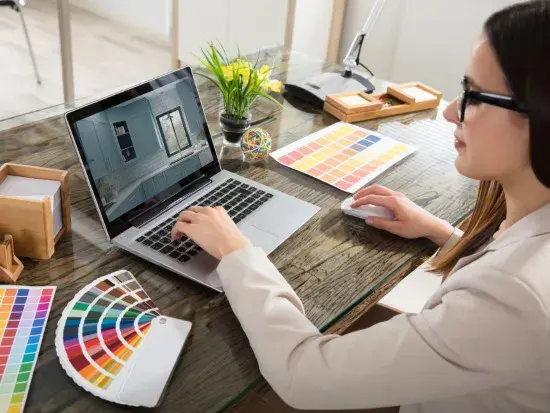 An image of a woman sitting at an open laptop creating a rendering of a kitchen.