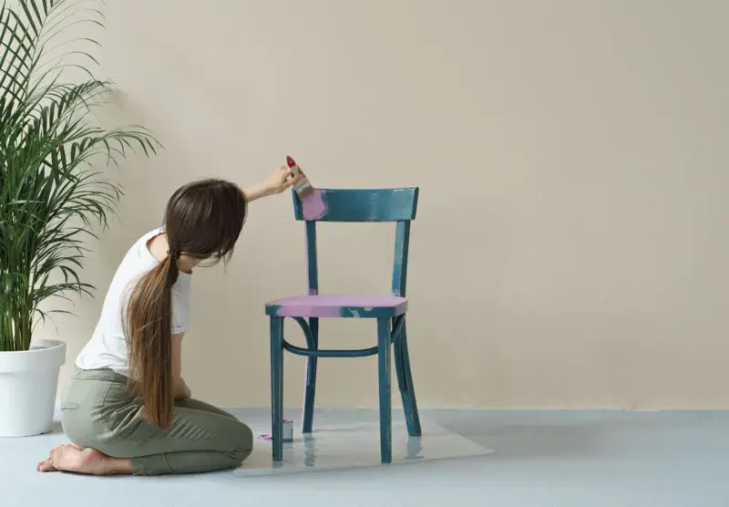 An image of a woman refinishing a chair by painting it with chalk paint.