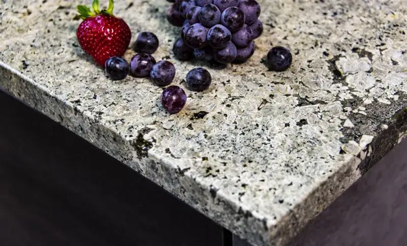 A closeup image of a brown granite countertop with strawberries and blueberries on the counter.