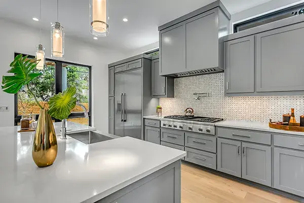 An image of a kitchen with grey cabinetry and metallic pulls, decorative lighting and quartz countertops.