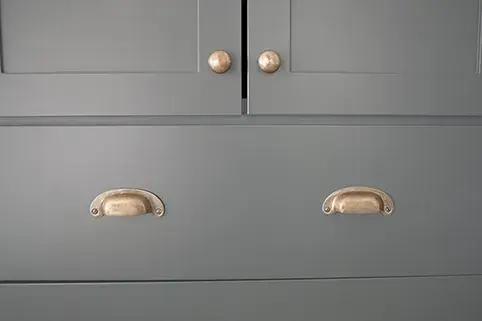 A closeup image of green cabinet doors and drawer fronts with brass knobs and cup pulls.