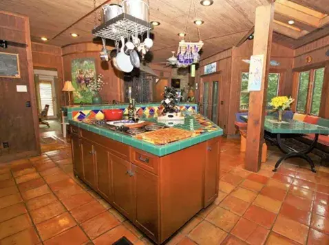 An image of an outdated kitchen in a lake house with tile countertops, oak cabinetry, and an Aztech inspired design.