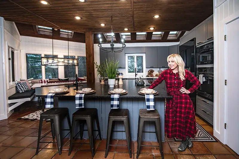 An image of Kortney Wilson standing in her newly renovated kitchen in a red and black checkered dress.
