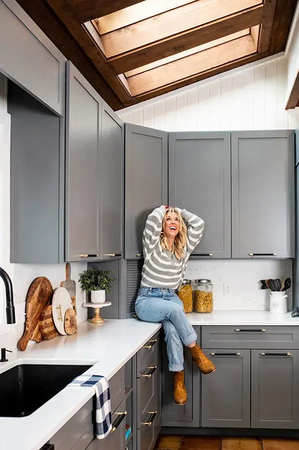 An image of Kortney Wilson sitting on her kitchen countertops smiling up towards the ceiling.