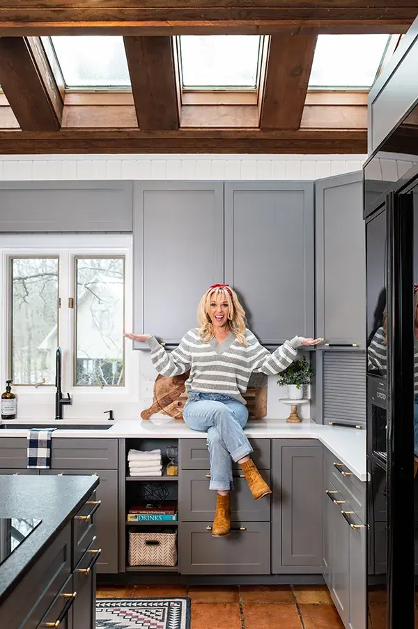 An image of Kortney Wilson sitting on her kitchen countertops showing off her new cabinet doors.