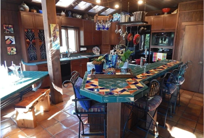 An image of a dated kitchen with honey oak cabinet doors, tile countertops, and a hanging pot rack.