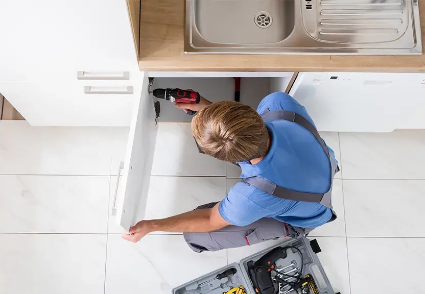 A photo of a man attaching a cabinet door hinge to a cabinet using a screwdriver.