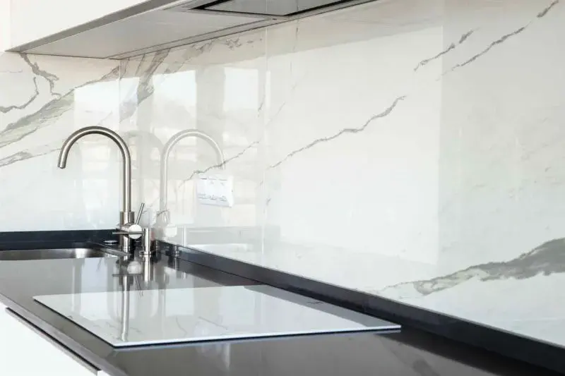 An image of a glossy marble backsplash slab behind a kitchen sink with a nickel faucet.