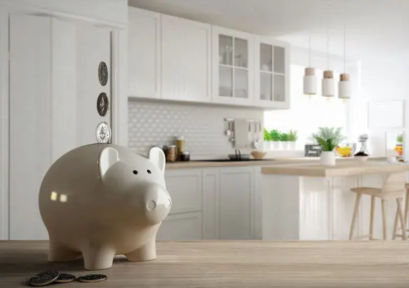 An image of a piggy bank with coins falling into it with a kitchen in the background.