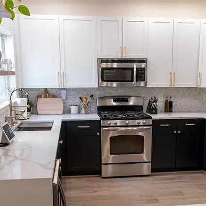 An image of a kitchen with black and white shaker cabinet doors, marble countertops, stainless steel appliances, gold hardware, and wooden floating shelves.