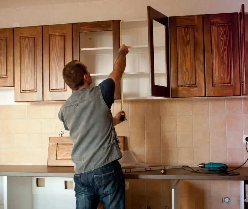 An image of a man hanging solid wood cabinet doors on upper cabinets in a kitchen.