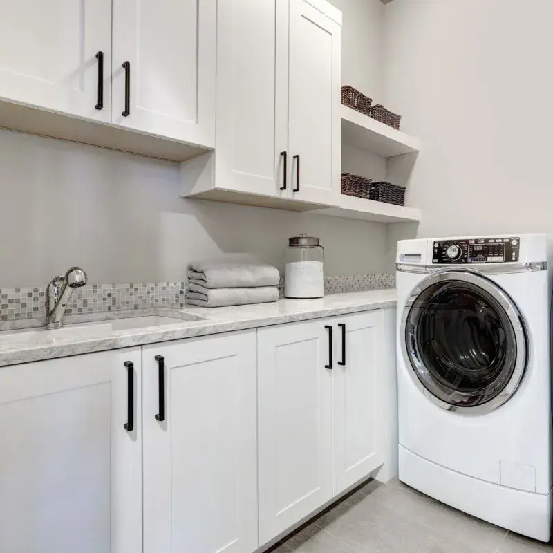 An image of a laundry room with white cabinetry and white floating shelves.
