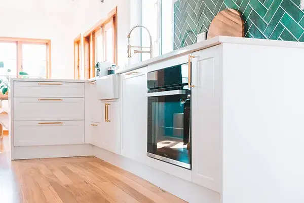 An image of white shaker style kitchen cabinetry with golden brass hardware.