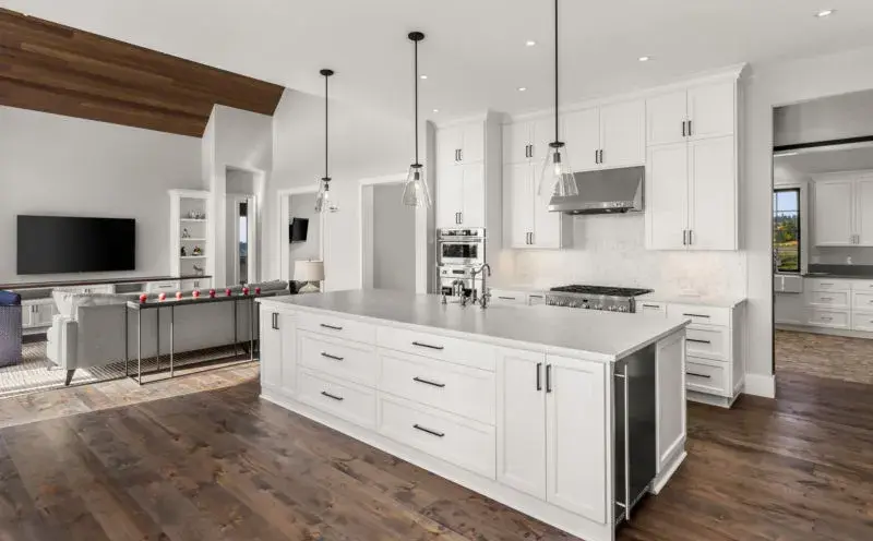 An image of a kitchen with white shaker cabinet doors,dark brown hardwood flooring, stainless steel applianes, and black hardware.